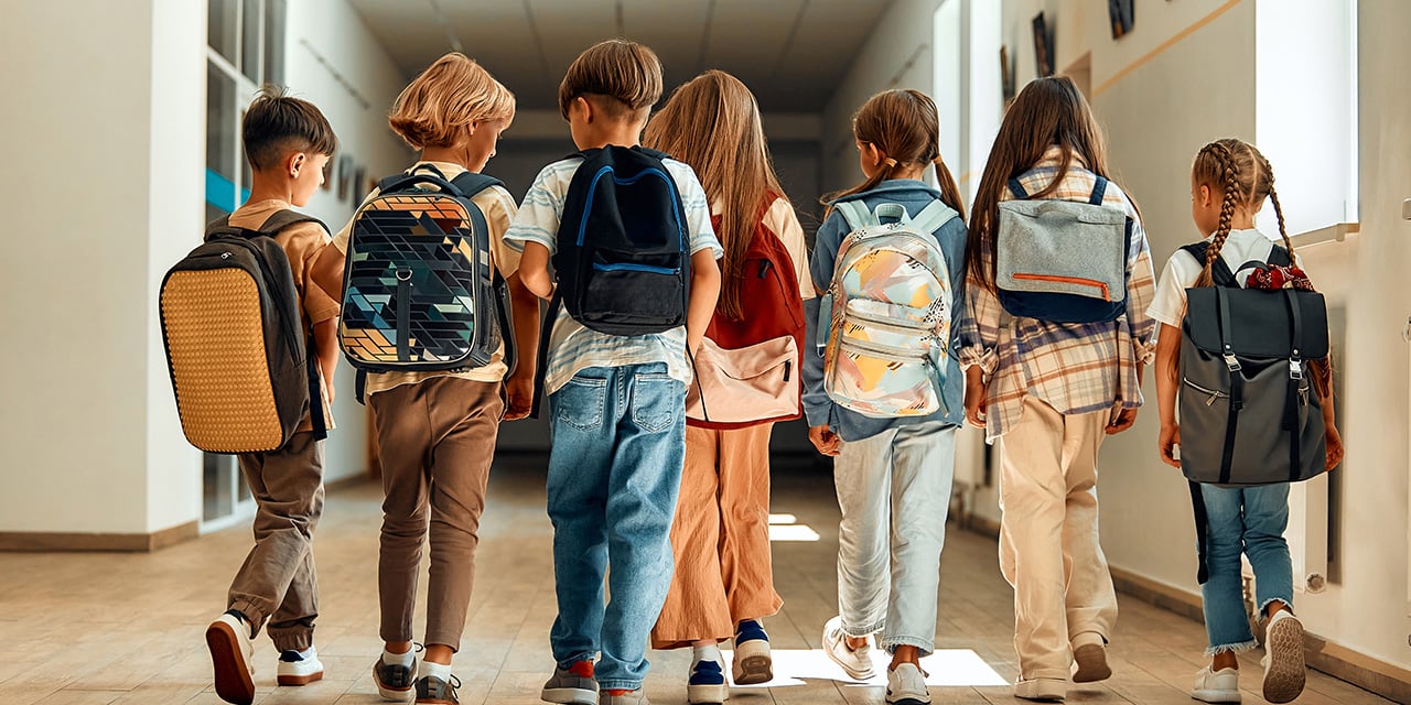 Children walking down school hallway wearing backpacks.