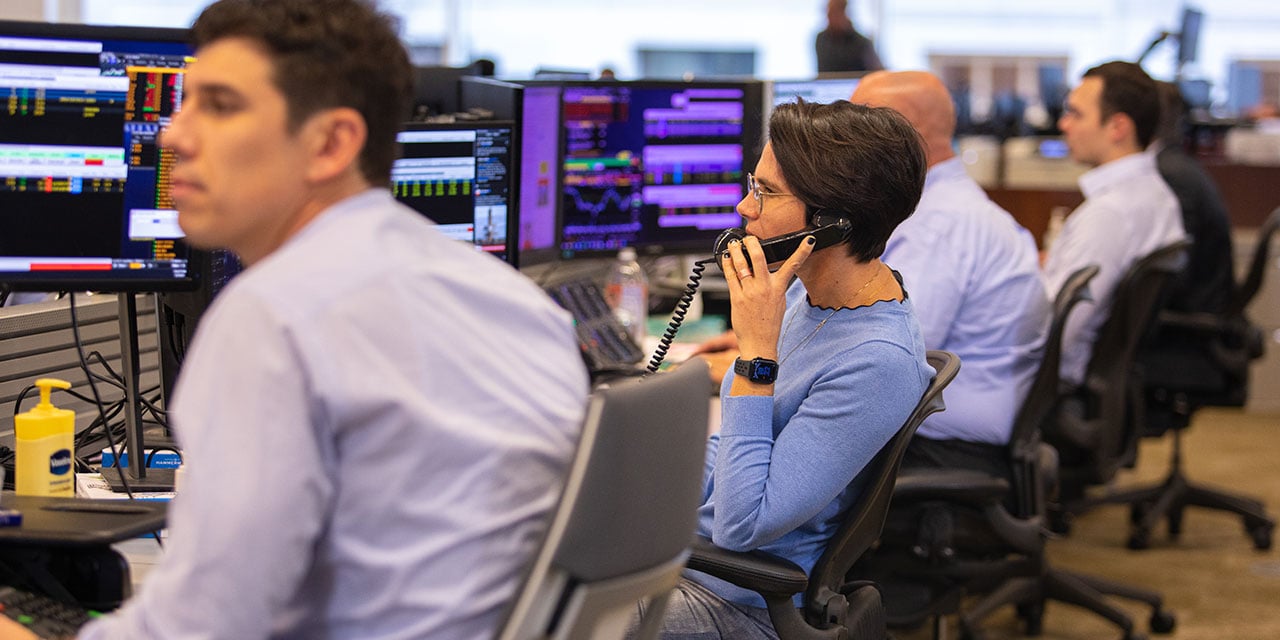 Four professionals working at terminals on a trading desk.