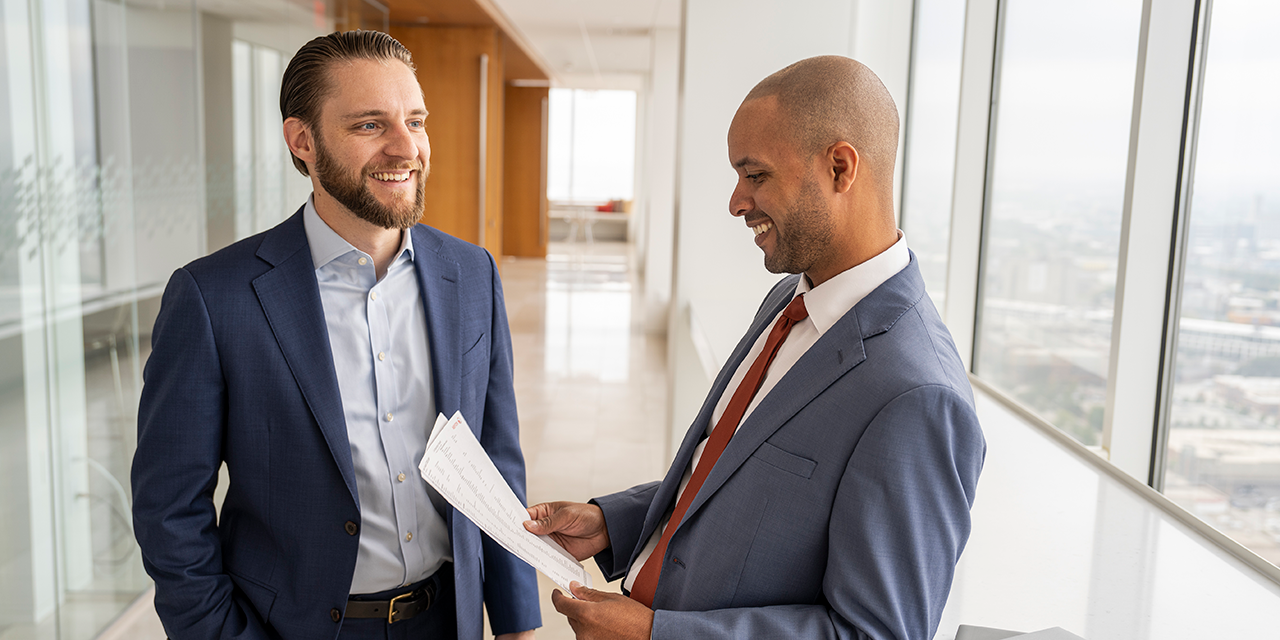 Two men in suits talking in a hallway of an office building.